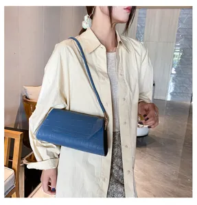 Nahaufnahme einer stilvollen blauen Kroko-Muster-Achseltasche, getragen vom Model in Innenräumen.