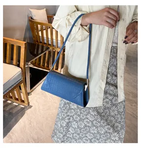 Detailansicht einer stilvollen blauen Umhängetasche mit Krokodilmuster am Model.