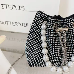 Close-up of black rhinestone bucket bag with elegant faux pearl handle and metal chain.