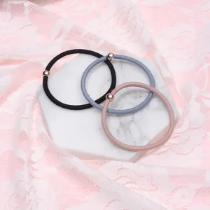 Close-up detail shot of minimalist hair ties with metal beads on marble plate and lace fabric.