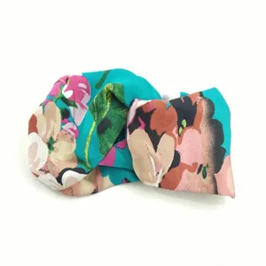 Gedetailleerd overzicht van de levendige bloemige satijnen elastische kruisende haarband in teal.