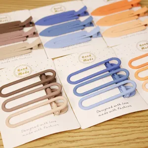 Close-up of minimalist pastel metal hair clips on cardboard display, smooth matte finish.