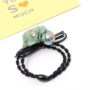 Elegant black hair tie detail featuring green fabric flower, pearls and bow decoration.