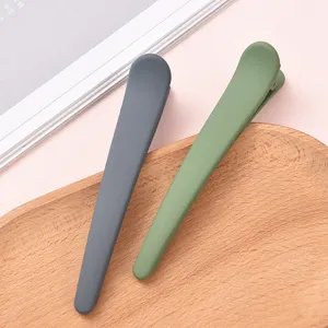 Matte finish large duckbill hair clips in dark gray and green, detail view on wooden tray.