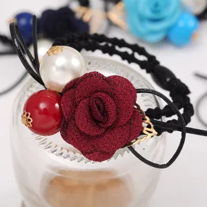 Detailed shot of a wine red fabric rose flower hair tie with large pearl and gold leaf.