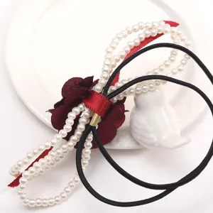 Detailed shot of elegant pearl string hair ring with red flower and black elastic band.