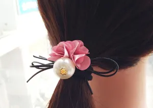 Closeup view of the elegant pink fabric flower and faux pearl hair tie detail worn on hair.