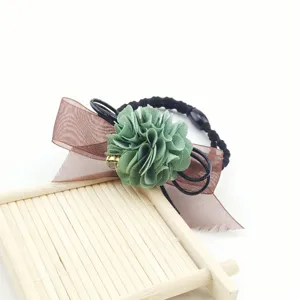 Detailed close-up of green fabric flower and brown organza bow hair tie detail view.