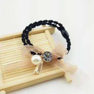 Close-up detail of black hair tie with sheer bow, pearl, and sparkling crystal pendant.