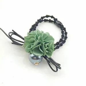 Close-up detail of the green fabric flower hair tie with grey pearl and black bow accent.