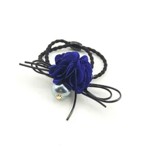 Detailed close-up of a dark blue fabric flower hair tie with a pearl and black cords.