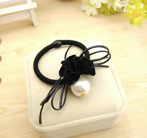 Detailed view of the black hair tie with fabric camellia flowers and large pearl decoration.