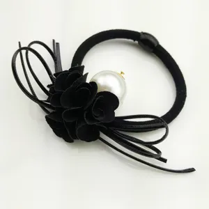 Close-up detail of black fabric camellia flower hair tie with pearl and bow decor.