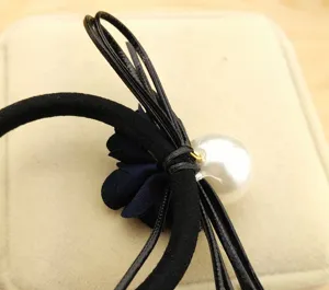 Close-up detail of black hair tie with blue flower and large pearl for stylish daily hairstyles.
