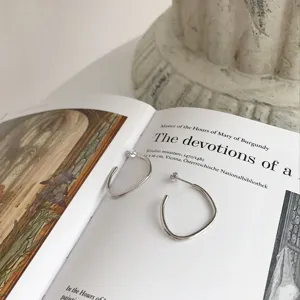 Silberne geometrische Herz-Ohrstecker auf Kunstbuch-Hintergrund, minimalistischer Vintage-Schmuck.