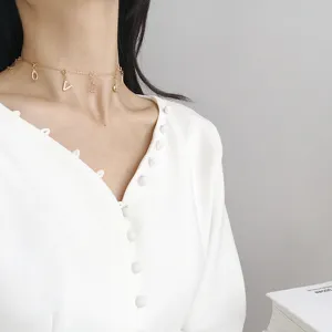 Nahaufnahme einer filigranen goldenen Choker-Halskette mit stylischen Buchstabenanhängern.