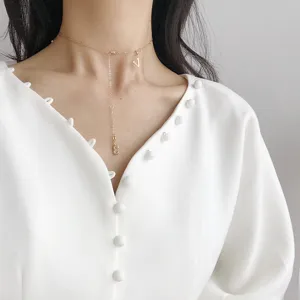 Filigrane goldfarbene Buchstaben und Zahlen Anhänger Halskette Detail im minimalistischen Stil.