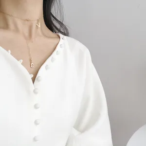 Nahaufnahme einer zarten Goldkette mit charmanten Buchstabenanhängern am Hals des Models.