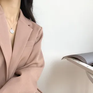 Detailansicht einer silbernen Münzketten-Halskette mit rosa Blazer für einen eleganten Look.