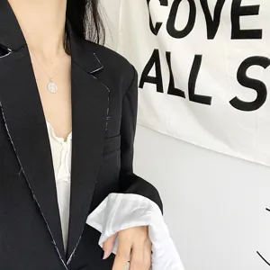 Close-up detail shot of retro silver coin pendant necklace worn with black blazer outfit.
