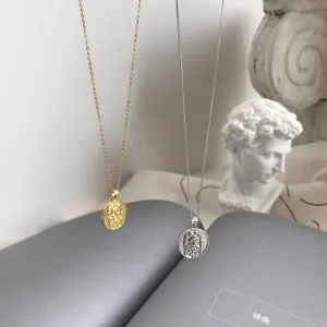 Nahaufnahme von Gold und Silber Münzanhänger Halsketten vor künstlerischem Buch und Skulptur.