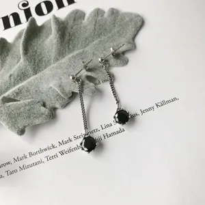 Close-up of silver dangle earrings with black zirconia stones and delicate chain design details.