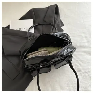 Detailed shot of black patent leather boston handbag interior capacity, dual handles & zipper.