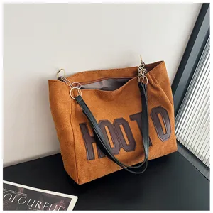 Classic brown suede tote bag with black handles and large letter patch, perfect for daily commuting.