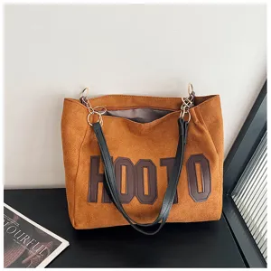 Detailed view of the brown suede tote bag with bold front lettering and black shoulder straps.