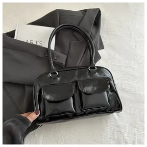 Black patent leather handbag detail showing dual front pockets, metallic hardware, and top handles.