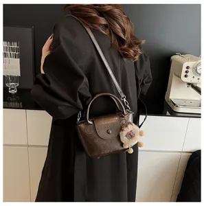 Detail view of vintage dark brown leather crossbody bag worn by model with plush charm.