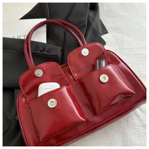 Glossy red shoulder handbag detail view, showing front flap pockets and metallic snap buttons.