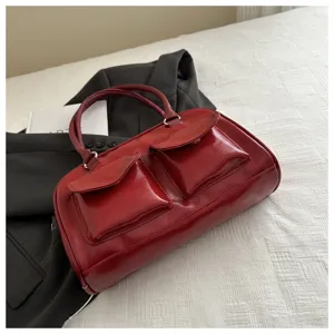 Detailed close-up of a vintage glossy red leather boston handbag with front pockets on white bed.