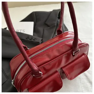 Red patent leather bowling handbag close-up showing double handles and front pocket details.