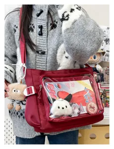 Clear front window of red Ita shoulder bag with cute plush pendant and badge display.