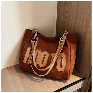 Brown suede tote bag detail, featuring durable shoulder straps and stylish front letter design.
