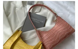 Detailed shot of trendy crocodile pattern baguette shoulder bags in pink and yellow colors.