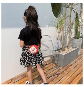 Detailed view of kids red round crossbody bag with cute white daisy flower design outdoors.