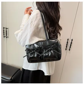 Detailed shot of black patent leather bowling shoulder bag with dual bow pockets.