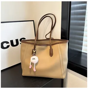 Detailed view of the beige tote bag featuring brown trim and a cute fluffy keychain decoration.