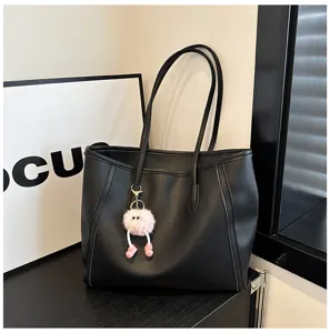 Black large capacity shoulder tote bag detail view with cute plush pompom charm accessory.