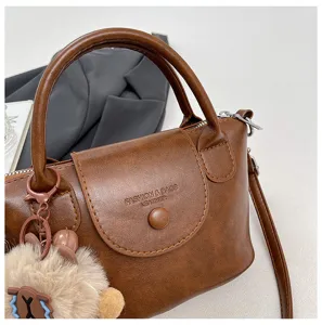 Brown leather top handle bag with cute plush bear pendant, elegant retro crossbody design.