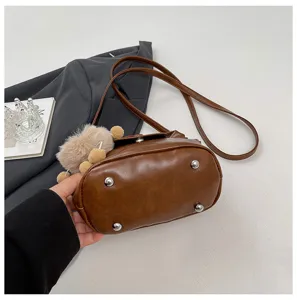 Detailed leather shoulder bag showing bottom metal feet and cute plush fluffy pendant charm.