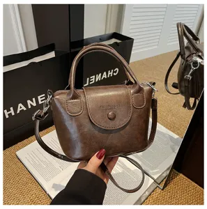 Detail shot of brown leather top-handle mini bag, vintage clasp closure design on open books.