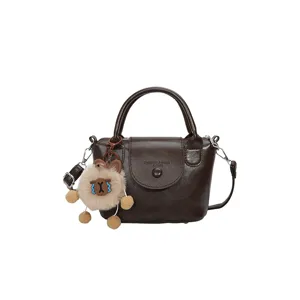 Mini dark brown leather top handle bag with crossbody strap and cute plush charm pendant.