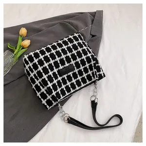 Detailed shot of a black and white houndstooth shoulder bag with chain strap and label.