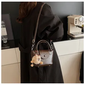 Detail view of the retro brown leather handbag featuring a cute furry charm and metal strap.