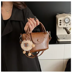 Brown leather crossbody bag detail, featuring fluffy plush charm and premium hardware design.