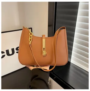Brown leather underarm shoulder bag detail featuring elegant golden chain and metal lock clasp.
