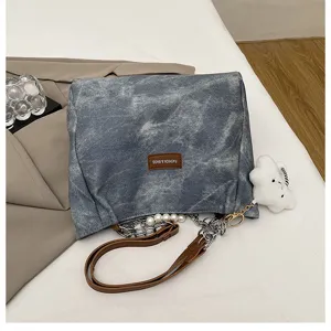 Close-up detail of casual denim shoulder tote bag with pearl chain and cute cloud pendant.